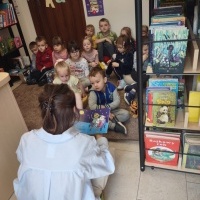 Filia nr 3  w Skrbeńsku. Na zdjęciu widoczne dzieci słuchające bajki, którą czyta pani bibliotekarka. Po prawej stronie widoczny regał z książkami.