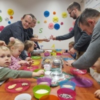 Na zdjęciu widoczna grupa osób w tym dzieci ozdabiających przy stołach pierniczki świąteczne. 