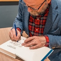 Mężczyzna podpisujący swoim autografem książkę.