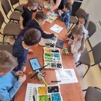 Grupa dzieci korzystających z tableta i budujących roboty z klocków Lego.