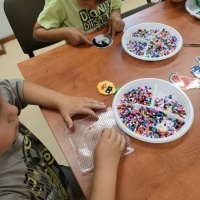 Widoczne dzieci siedzące przy stole i tworzące z koralików różne elementy.