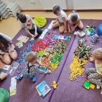 Grupa dzieci bawiąca się na dywanie klockami LEGO.