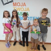 Dzieci stojące przy ścianie i prezentująca swoje wykonane budowle z klocków LEGO.