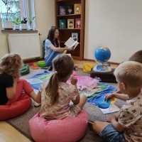 Dzieci siedzące na dywanie, które słuchaja opowiadania, które czyta pani bibliotekarka.