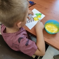 Chłopiec siedzący przy stole i wykonujący pracę plastyczną.
