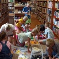Dzieci bawiące się klockami LEGO pomiędzy regałami z książkami.